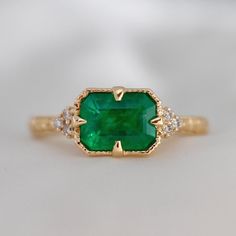 an emerald and diamond ring is shown on a white surface with gold trimmings