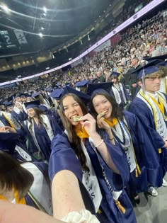 graduates in cap and gowns smile as they sit on the bleachers at graduation