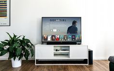 a flat screen tv sitting on top of a white entertainment center next to a potted plant