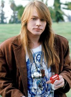 a young man with long hair holding a drink and an object in his right hand