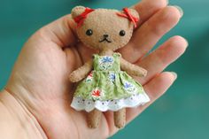 a small teddy bear in a green dress is being held by someone's hand