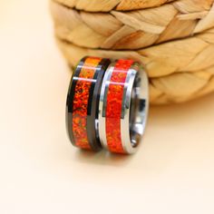 two rings with red and orange inlays are sitting next to a woven basket