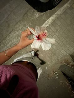 a person holding a flower in their hand on the sidewalk next to a parked car