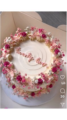 a white cake with pink flowers on it in a box that says love spelled out