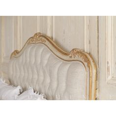 a white bed with gold trim and headboard in a room that has peeling paint on the walls