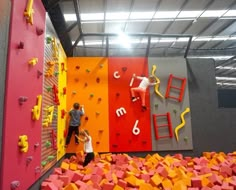 two children are climbing up and down the wall in an indoor climbing area with colorful walls