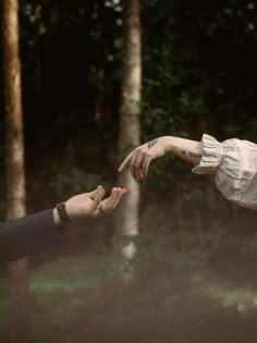 two people reaching out their hands to touch each other in front of some trees and grass