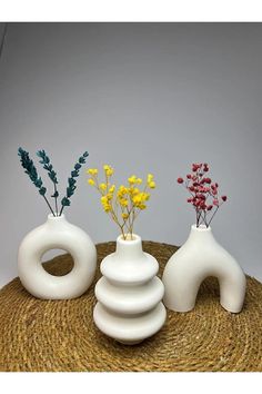 three white vases with flowers in them on top of a straw hat covered table