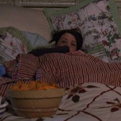 a woman laying in bed next to a bowl of food