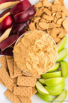 an assortment of snacks including apples, crackers and peanut butter on a white plate