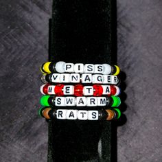 four different colored beads are on top of a black piece of paper that says, piss vintage metal swarm rats