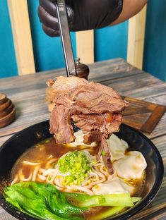 a person is cutting into some meat with broccoli and noodles in a bowl