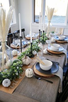 the table is set for thanksgiving dinner with white pumpkins, greenery and candles