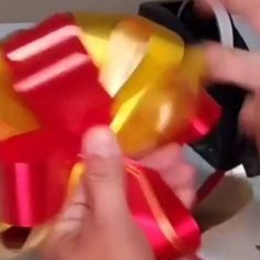 the person is holding a red and yellow gift box with ribbons on it's sides