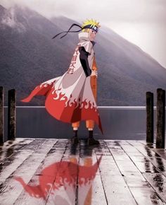 a man standing on top of a wooden dock next to water and mountains in the background