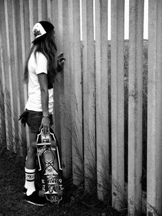 a girl leaning against a wooden fence with her skateboard and helmet on, looking at the wall