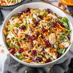 a salad with chicken, cranberries and nuts in a white bowl on a marble table