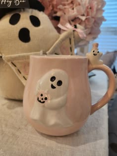 a pink coffee mug with a ghost face on it and a stuffed animal in the background