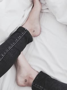 a person laying in bed with white sheets and black jeans on their feet, under the covers