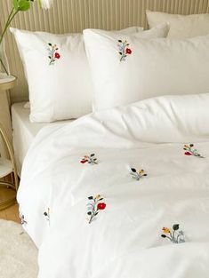 a bed with white linens and embroidered flowers on it, along with two side tables