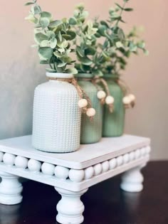 three vases with flowers are sitting on a small white table and one has green leaves in it