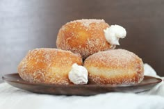 three sugared donuts on a plate with whipped cream toppings and powdered sugar