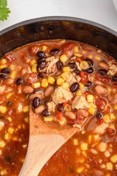 a wooden spoon in a pot filled with beans and chicken