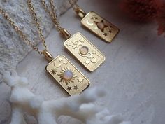 two gold necklaces sitting on top of a white rock next to a red flower