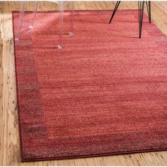 a red area rug with an acrylic chair in the background and wood flooring