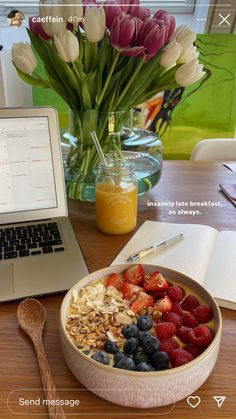 a bowl of fruit and cereal next to a laptop