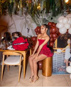 a woman in a red dress sitting at a table with balloons hanging from the ceiling