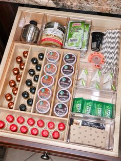 an open drawer with various items in it on a wooden table next to a marble counter top