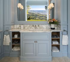 a bathroom with blue cabinets and white marble counter tops, along with an open window