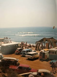 many cars are parked on the beach by the ocean and people in the water behind them