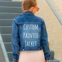 a woman wearing a jean jacket with the words custom painted on it, standing in front of some stairs