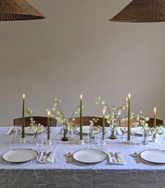 the table is set with white plates and silverware, candles and flowers in vases