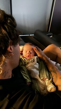 a man holding a baby in his arms with tattoos on it's chest and arm