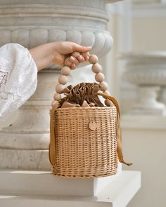 a person holding a wooden bead in a wicker basket on top of a white pedestal