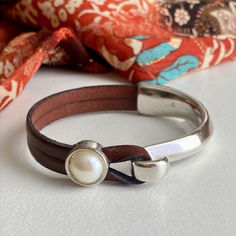 a close up of a bracelet on a table with a scarf in the back ground