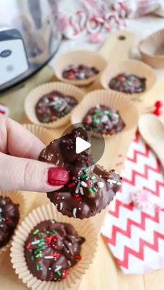 someone holding up some chocolates in their hand on a table with other food items