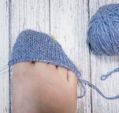 a baby's foot next to a ball of yarn on a white wooden floor