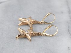 The perfect wardrobe basic, these diamond textured gold starfish drop earrings are comfortable and versatile! These gorgeous, classic earrings will transition easily from day to night. Metal: 14K Yellow Gold Gem: 2 Diamonds totaling .26 Carats, G in Color, SI1 in Clarity Gem Measurements: 3.2 mm, Round Earrings Length: 40 mm Earrings Width: 21 mm Marks: “ZB 14K” Stamped on the Findings Gold Elegant Earrings With Starfish Charm, Elegant Gold Earrings With Starfish Charm, Elegant Starfish Charm Drop Earrings, Yellow Gold Starfish Earrings With Starfish Charm, Elegant Yellow Gold Earrings With Starfish Charm, Elegant Yellow Gold Starfish Charm Earrings, Starfish Jewelry, Starfish Earrings, Nautical Jewelry