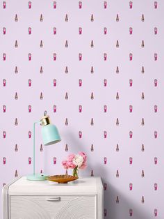 a white dresser with a lamp and pink wallpaper