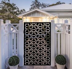 a white fence with two potted plants next to it and a black iron gate