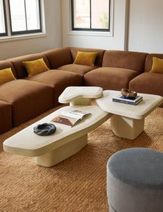 a living room filled with lots of furniture next to two large windows on top of a brown carpeted floor