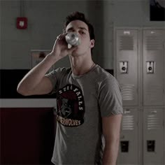 a man standing in a locker room drinking from a bottle