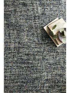 an area rug with a book on top and a plant next to it in the middle