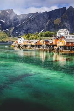 the water is crystal green and clear with houses on it, along with mountains in the background