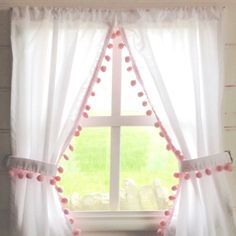 a window with pink pom poms hanging from it's sides and a white curtain