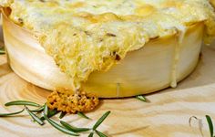 a cheesy casserole on a wooden platter with rosemary sprigs